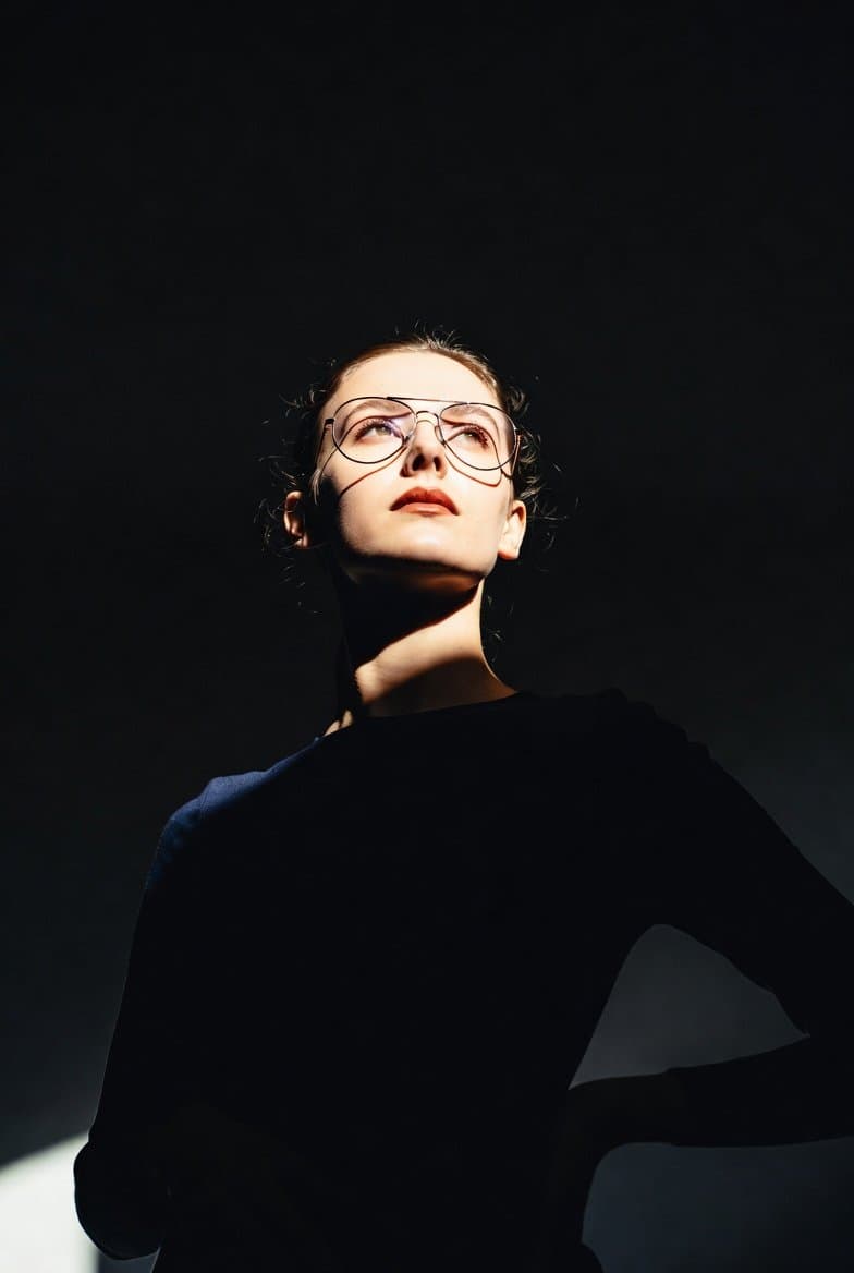 A dramatic, low-angle portrait of a woman standing in a dark, minimalist spac...