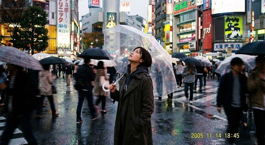 Tokyo Street Crossing A grainy digital photo shows a young woman in a trench ...